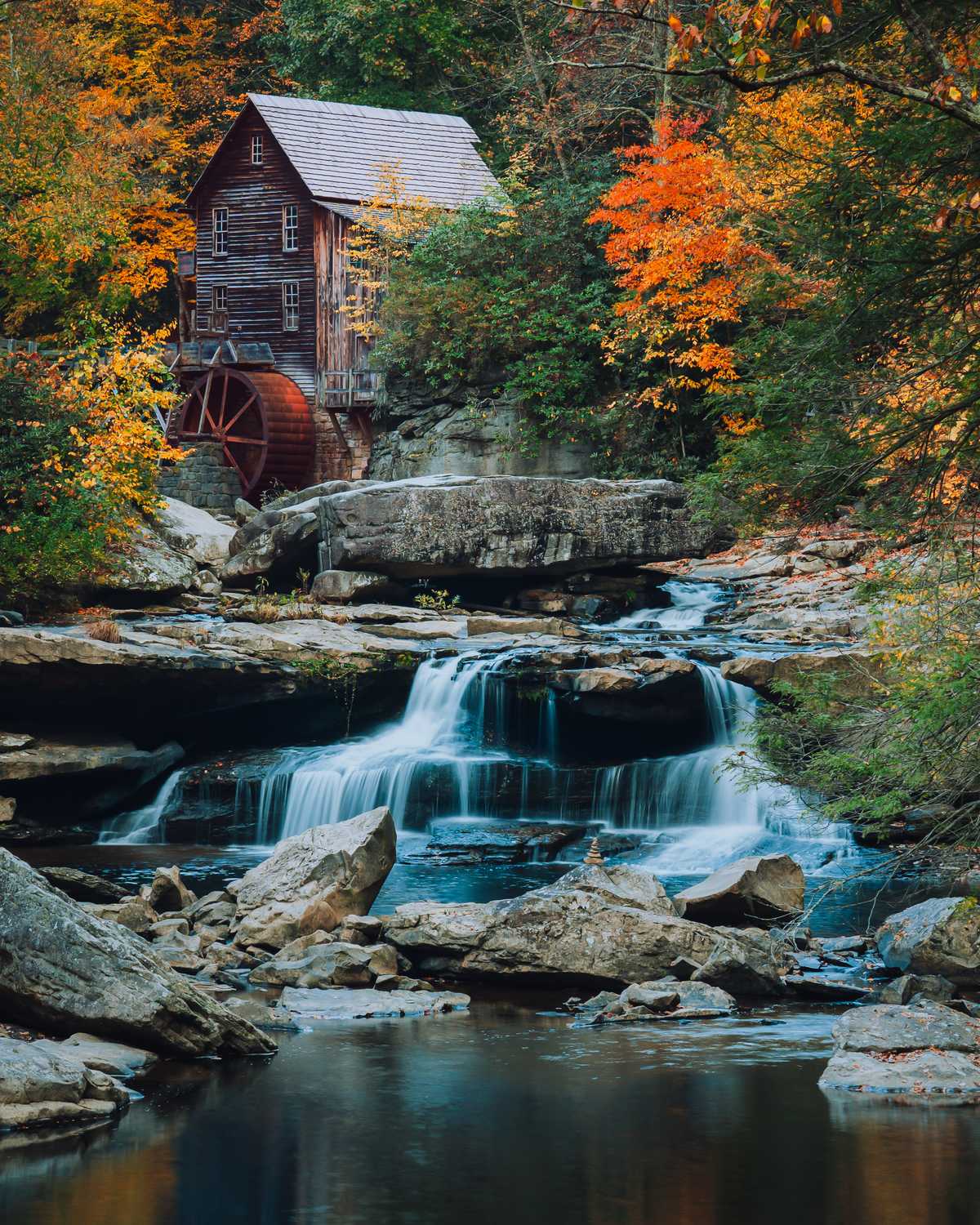 An autumn waterfall in front of Glade Creek Grist Mill surrounded by yellow and orange foliage