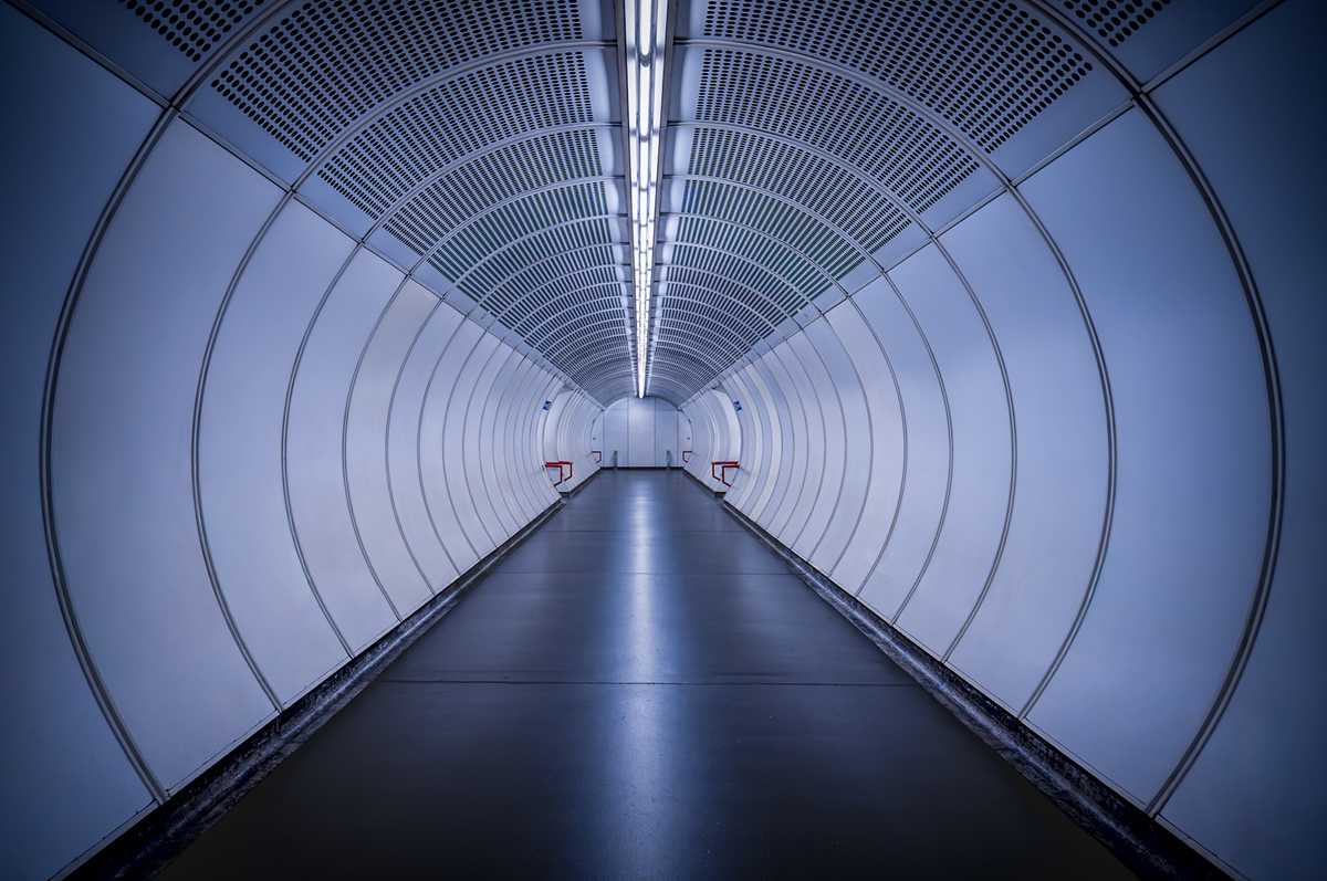 A symmetric futuristic pedestrian tunnel with white curved panels and blue accents leading to a vanishing point